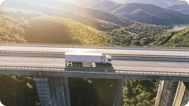 Caminhão atravessando uma ponte em local arborizado