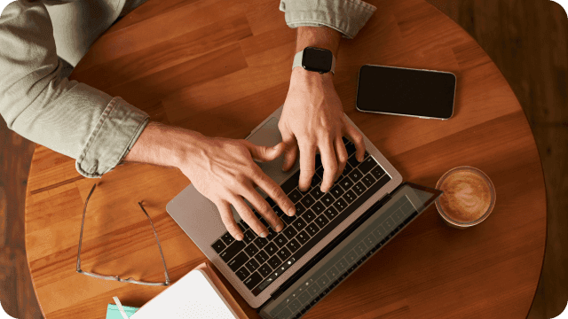 Mãos masculinas digitando em um notebook sobre a mesa